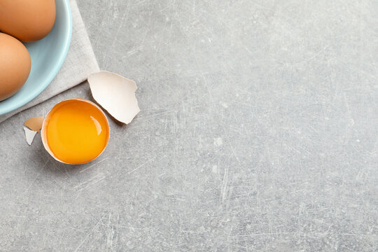 Raw chicken eggs and shell with yolk on light grey table, flat lay. Space for text