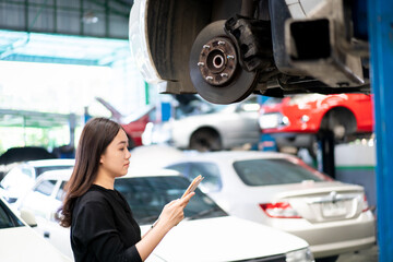 Asian young woman in black shirt examining a vehicle suspension and break system in garage.