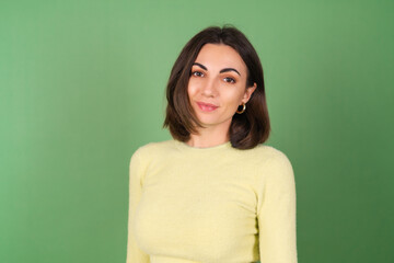Obraz premium Young woman on a green background in a yellow sweater cute smiling