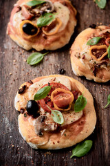 Mini Pizzas with mozzarella cheese, cherry tomatoes, black olives and fresh basil. Dark background. Close up.	