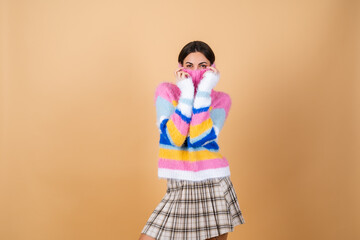 Young woman on a beige background in a bright multicolored cozy knitted sweater and a plaid skirt smiling cute