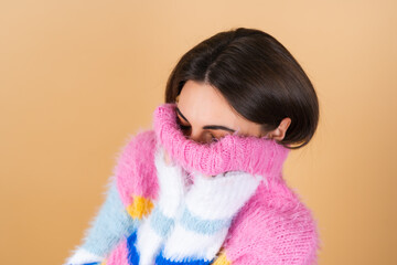 Young woman on a beige background in a bright multicolored cozy knitted sweater cute smiling