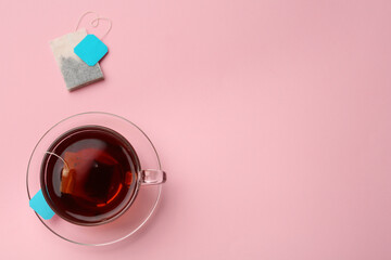 Tea bags and cup of hot drink on pink background, flat lay. Space for text