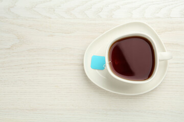 Obraz premium Tea bag in ceramic cup of hot water on white wooden table, top view. Space for text
