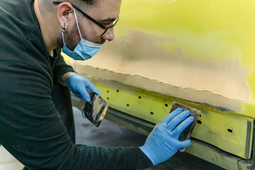 Auto mechanic repairing a yellow car with putty for paint in a workshop