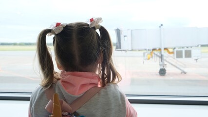 little girl aged 5 years looks out the window at the airport, waiting for the departure or arrival of the plane, dreaming of a trip