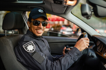 Police officer in sunglasses poses in patrol car