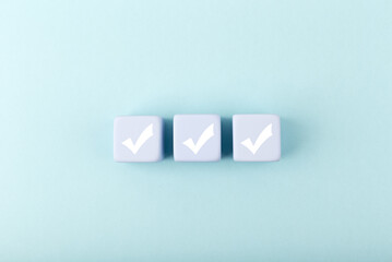 Three white checkmarks on blue toy cubes in a row on bright pastel blue background with copy space