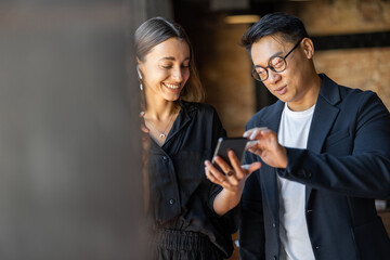 Smiling multiracial business people talking during work in cafe. Concept of remote and freelance work. Idea of teamwork and business cooperation. European woman and asian man near window indoors