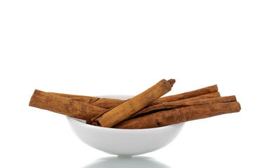 Several fragrant dry cinnamon sticks in a white ceramic saucer, close-up, isolated on white.