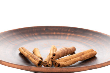 Several fragrant dry cinnamon sticks on a clay plate, close-up, isolated on white.