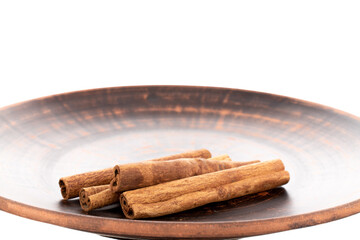 Several fragrant dry cinnamon sticks on a clay plate, close-up, isolated on white.