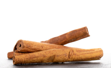 Three fragrant dry cinnamon sticks on a slate stone, close-up, isolated on white.