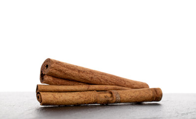 Two fragrant dry cinnamon sticks on a slate stone, close-up, isolated on white.