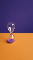 hourglass from transparent glass on a purple and orange background.