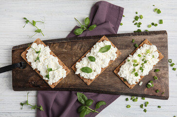 Crispy crackers with cottage cheese and different herbs on white wooden table, flat lay