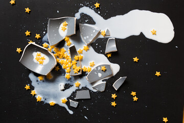 broken ceramic cup with food: dried cornflakes stars and milk on black background. concept of...
