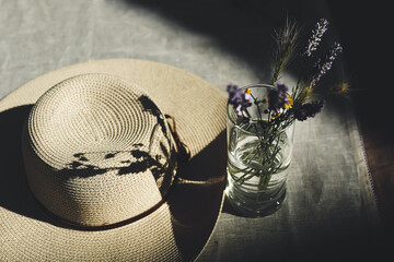Wildflowers in the glass with water and womens summer hat on a table covered with linen tablecloth...