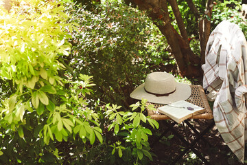 An open book and women's summer hat on old wicker chair in garden, provence and nature slow life...