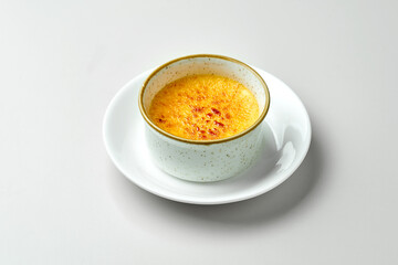 Dessert creme brulee in a white plate on a gray background.