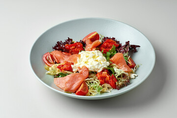 Diet salad with salmon and stracciatella cheese in a gray plate on a white plate