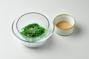 Diet salad of wakame (chuka) seaweed and nuts sauce in a gray plate on a white background