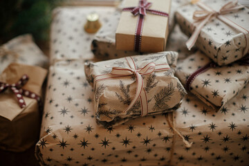 Stylish christmas gifts wrapped in craft paper, fir branches and bells on rustic wood. Stylish scandinavian xmas presents, atmospheric winter time in countryside. Merry Christmas!