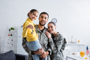 Cheerful parents in military uniform holding daughter with key at home
