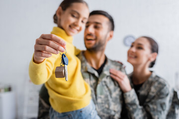 Blurred parents in military uniform holding daughter with key at home - Powered by Adobe