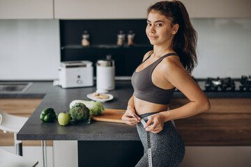 Young woman with measuting tape on weist at the kitchen