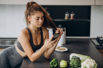 Sporty woman at kitchen using mobile phone