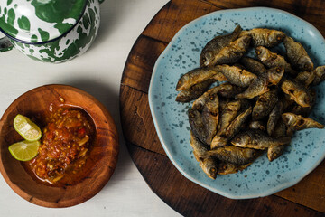 fried baby fish with hot and spicy sauce and cantella asiatica as side dish on wooden board against white background
