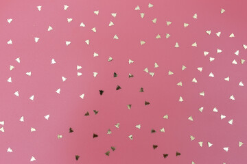 Fototapeta na wymiar scattered golden confetti in the shape of Christmas trees on a pink background
