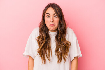 Young caucasian woman isolated on pink background shrugs shoulders and open eyes confused.