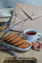 Oatmeal cookies with hot tea on a natural wood kitchen board. Winter composition for the interior with snow-covered branches and rowan berries. Vertical photo in actual shades of brown.
