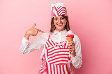 Young ice cream maker woman holding ice cream isolated on pink background person pointing by hand...