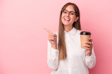 Young business caucasian woman holding a take away isolated on pink background smiling and pointing aside, showing something at blank space.