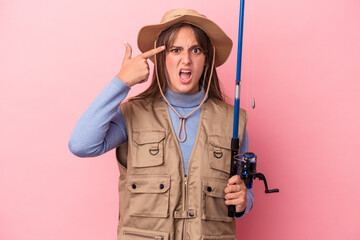 Young caucasian fisherwoman holding a rod isolated on pink background showing a disappointment gesture with forefinger.