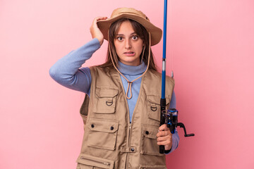 Young caucasian fisherwoman holding a rod isolated on pink background being shocked, she has remembered important meeting.
