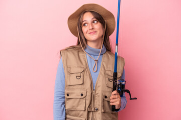 Young caucasian fisherwoman holding a rod isolated on pink background dreaming of achieving goals and purposes