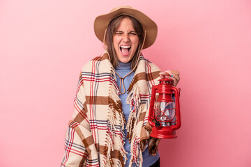 Young caucasian woman holding vintage lantern isolated on pink background screaming very angry and aggressive.