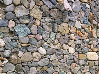 A wall of stones of different colors. Multicolored stones are stacked on top of each other. A stone wall.