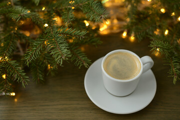 Obraz na płótnie Canvas Christmas or winter coffee. Coffee cup, Christmas tree and Christmas lights, golden bokeh, blurred background. Black coffee atmosphere of winter festive and hot aroma drink at a wintertime, new year