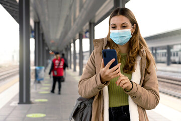 Beautiful young woman wearing medical mask ready to shows her sanitary passport on smartphone to...