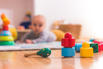 Baby toddler playing concept: Colorful rattle and blocks in the foreground, playing baby in the blurry background