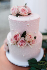 Beautiful pink wedding cake with fresh roses stands on the table Traditional Two-tier wedding cake decorated with roses on the top Pink roses on the pink wedding cake isolated Close up