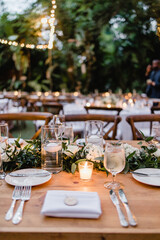 Wooden wedding table decorated with Greenery, white candles Served table for dinner on the wedding party at the luxury hotel restaurant table set up for a special event with lit candles in glasses 