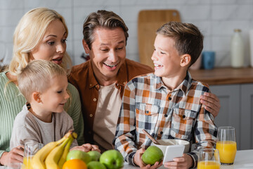 boy holding smartphone during breakfast with brother and cheerful parents