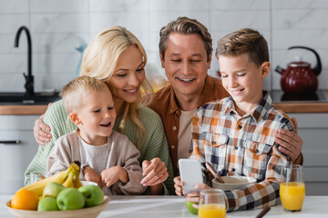 smiling boy showing smartphone to happy family during breakfast