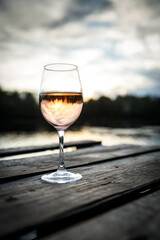 Sunset view of a glass of orange wine on a wooden pier on a lake.